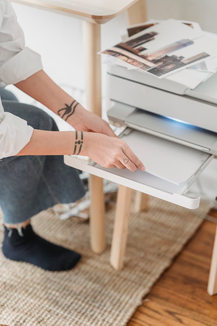 Close-up of a woman with tattoos using a printer at home, capturing freelance work environment.